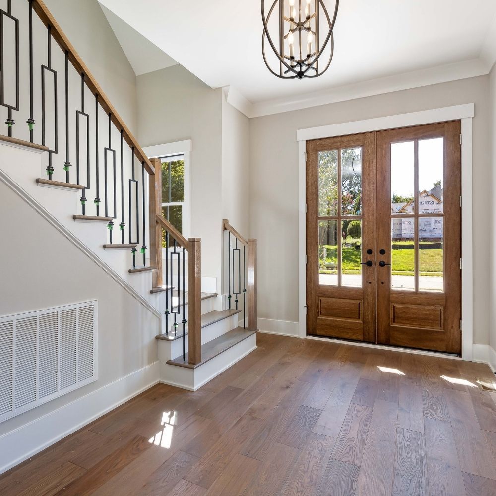 Bright foyer with wood flooring, a staircase featuring metal railings, and double wooden front doors with glass panes.