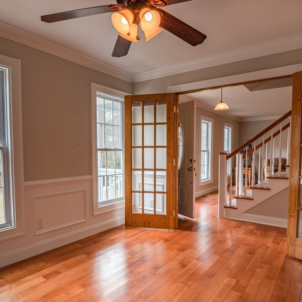 Light-filled room with hardwood floors, a ceiling fan, and French doors opening to a staircase in the next room.