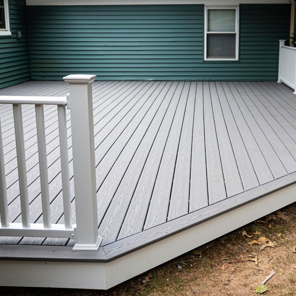 A light gray composite deck with white railings attached to a house with dark green horizontal siding.