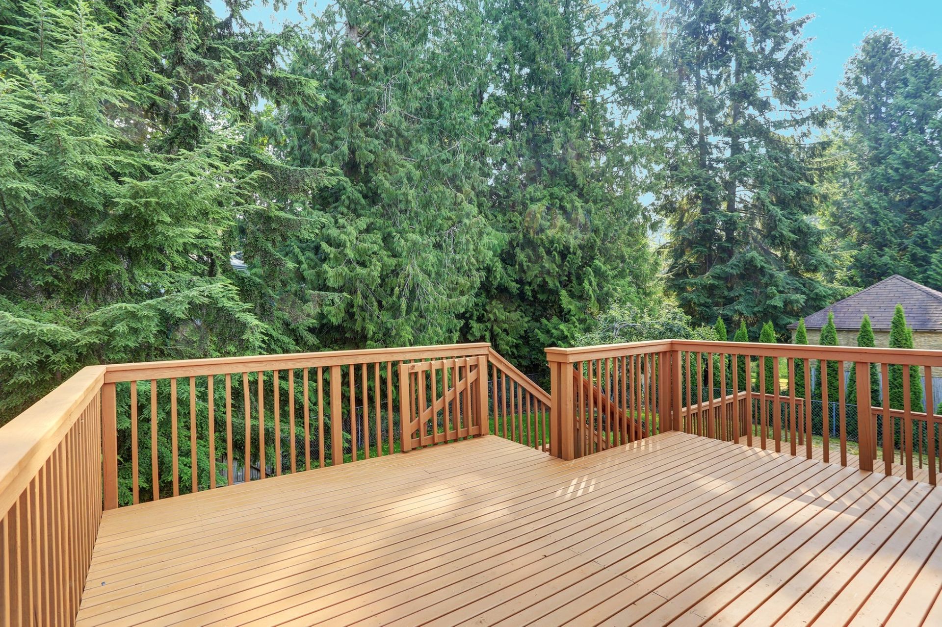 A wide wooden deck with railings, overlooking a lush green forest on a sunny day.