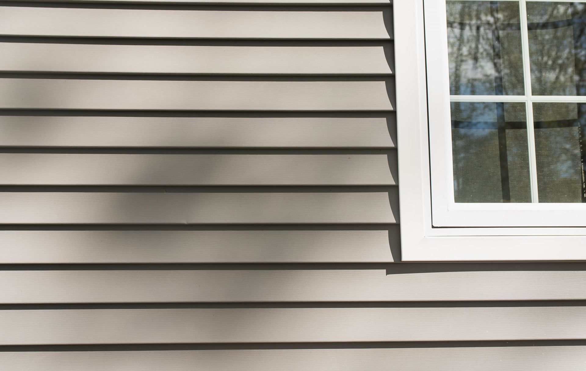 Gray horizontal vinyl siding on a building wall next to a white-framed window.