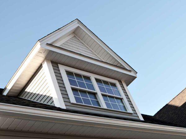 A gabled dormer window with gray siding and white trim against a clear blue sky.