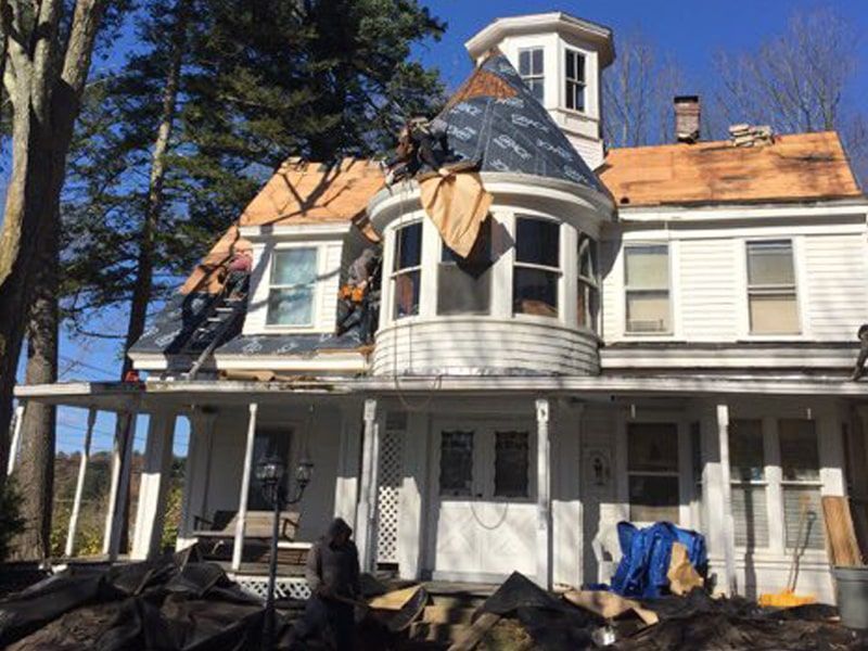 Roofers working on a two-story white house with a round tower section under construction on a sunny day.