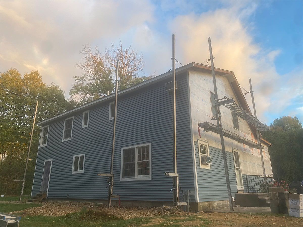A side view of a two-story house undergoing renovations, featuring partial blue siding, scaffolding, and a white facade.