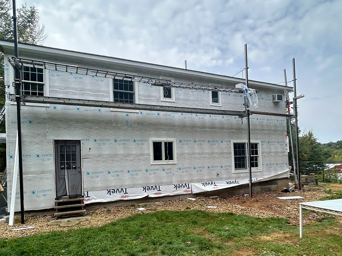 A two-story building under renovation, wrapped in white Tyvek weather-resistant barrier, surrounded by metal scaffolding.