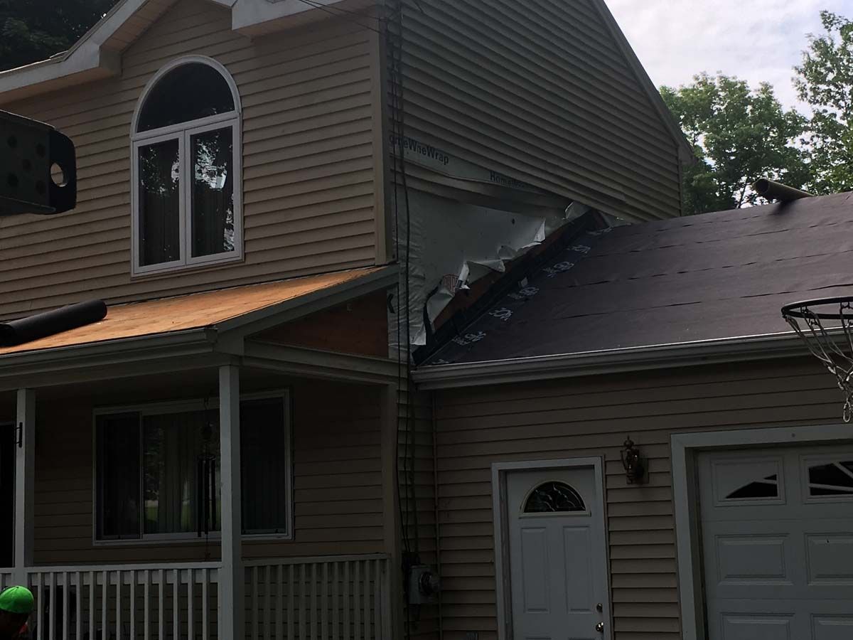 A beige house with tan vinyl siding showing a large gap and exposed insulation where a garage roof joins the main wall.
