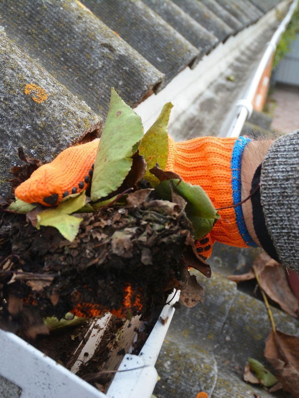 A person wearing orange gloves is cleaning a gutter