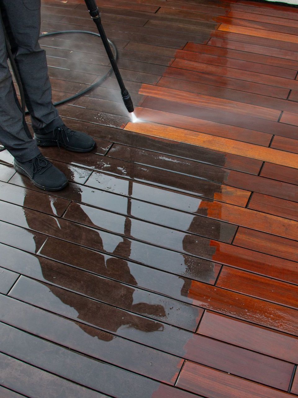 A person is cleaning a wooden deck with a high pressure washer.