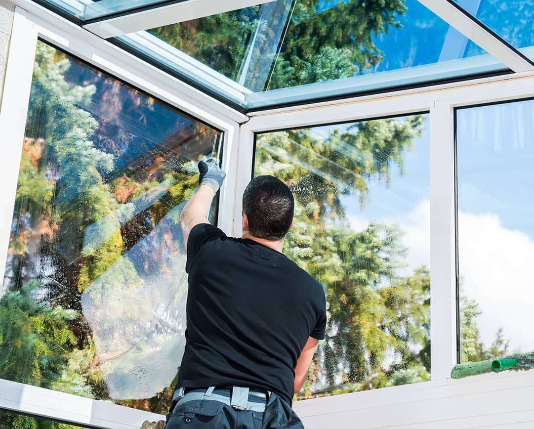 A man is cleaning a window in a conservatory.
