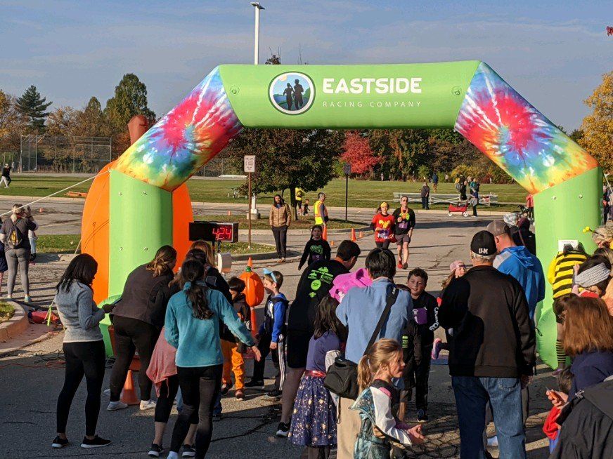 Runners crossing the finish line under an inflatable archway at an Eastside Running Company event. Spectators watch from the sidelines.