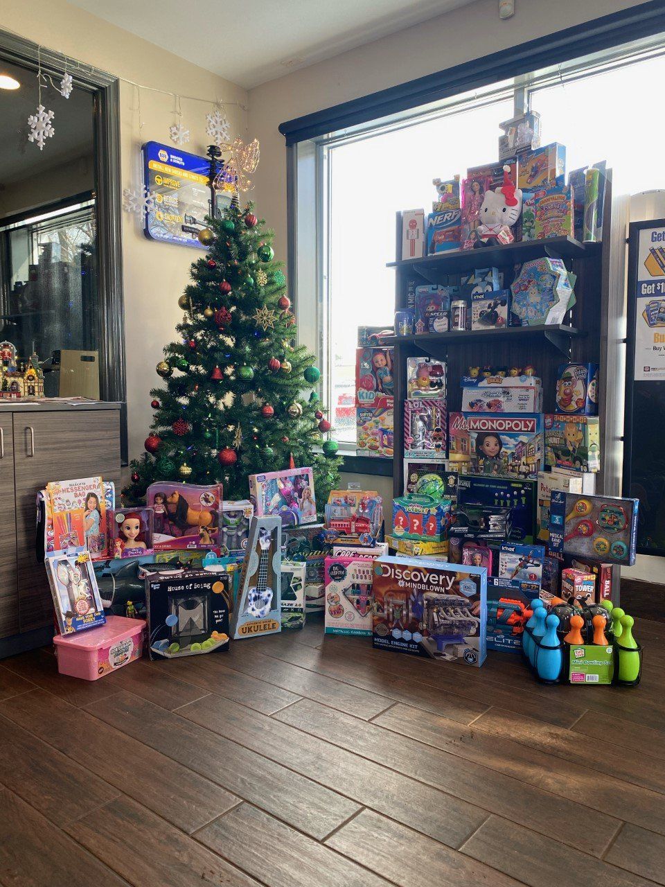 A decorated Christmas tree and a large collection of wrapped gifts and toys are displayed in a room with wooden floors.