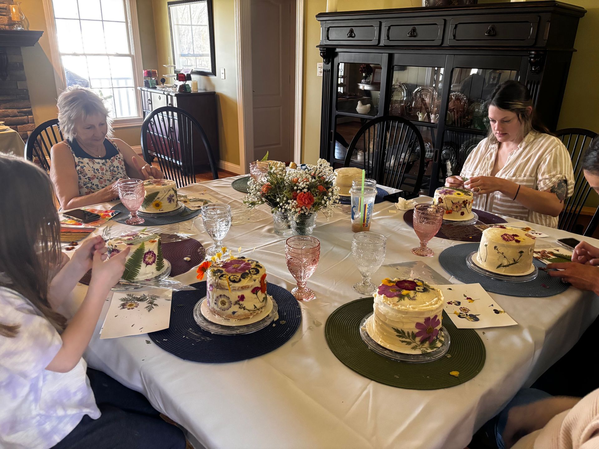 Five people decorate cakes in a kitchen. They use piping bags with colorful frosting, smiling.