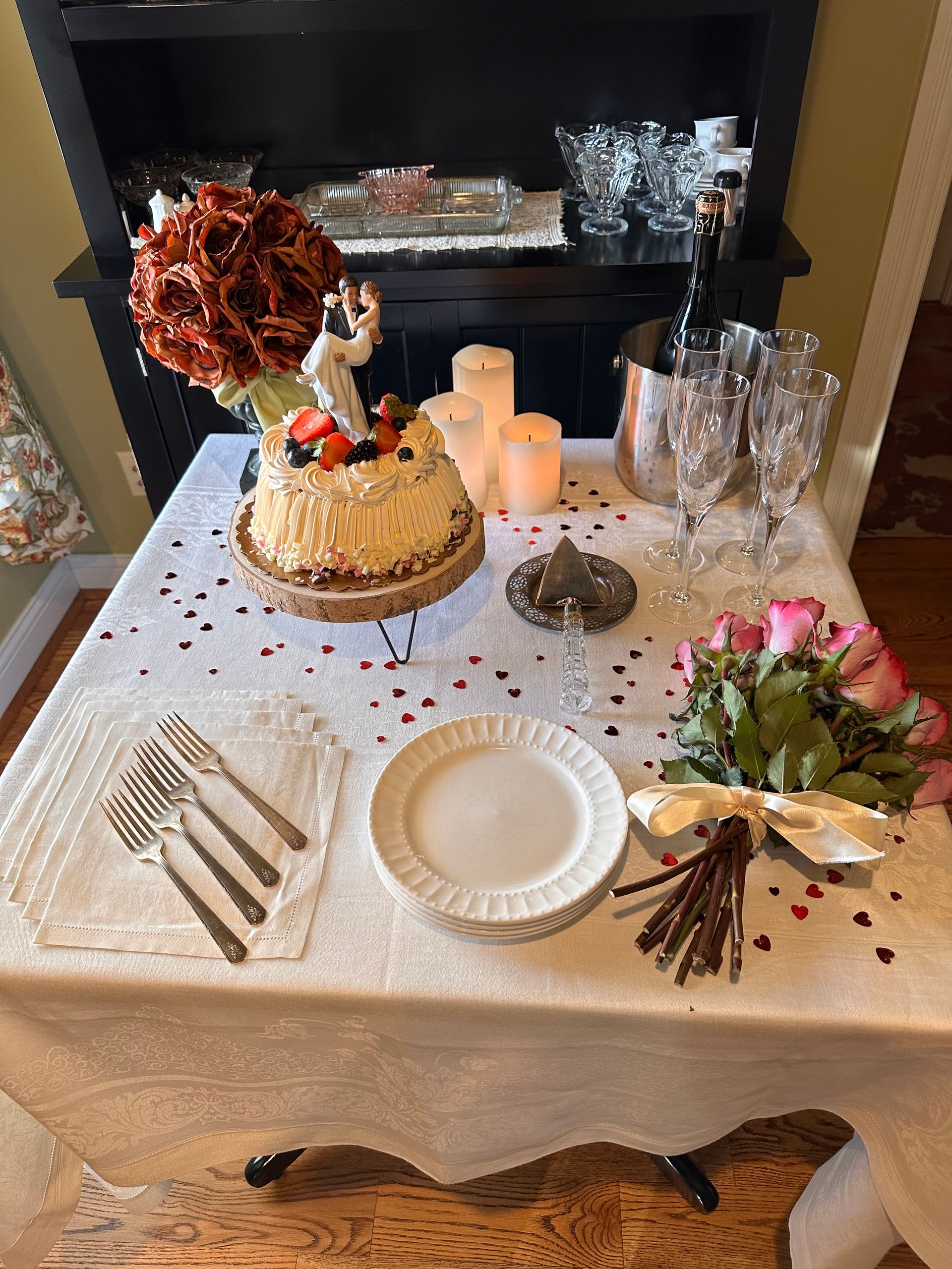 A table with plates , utensils , a cake , candles and flowers on it.
