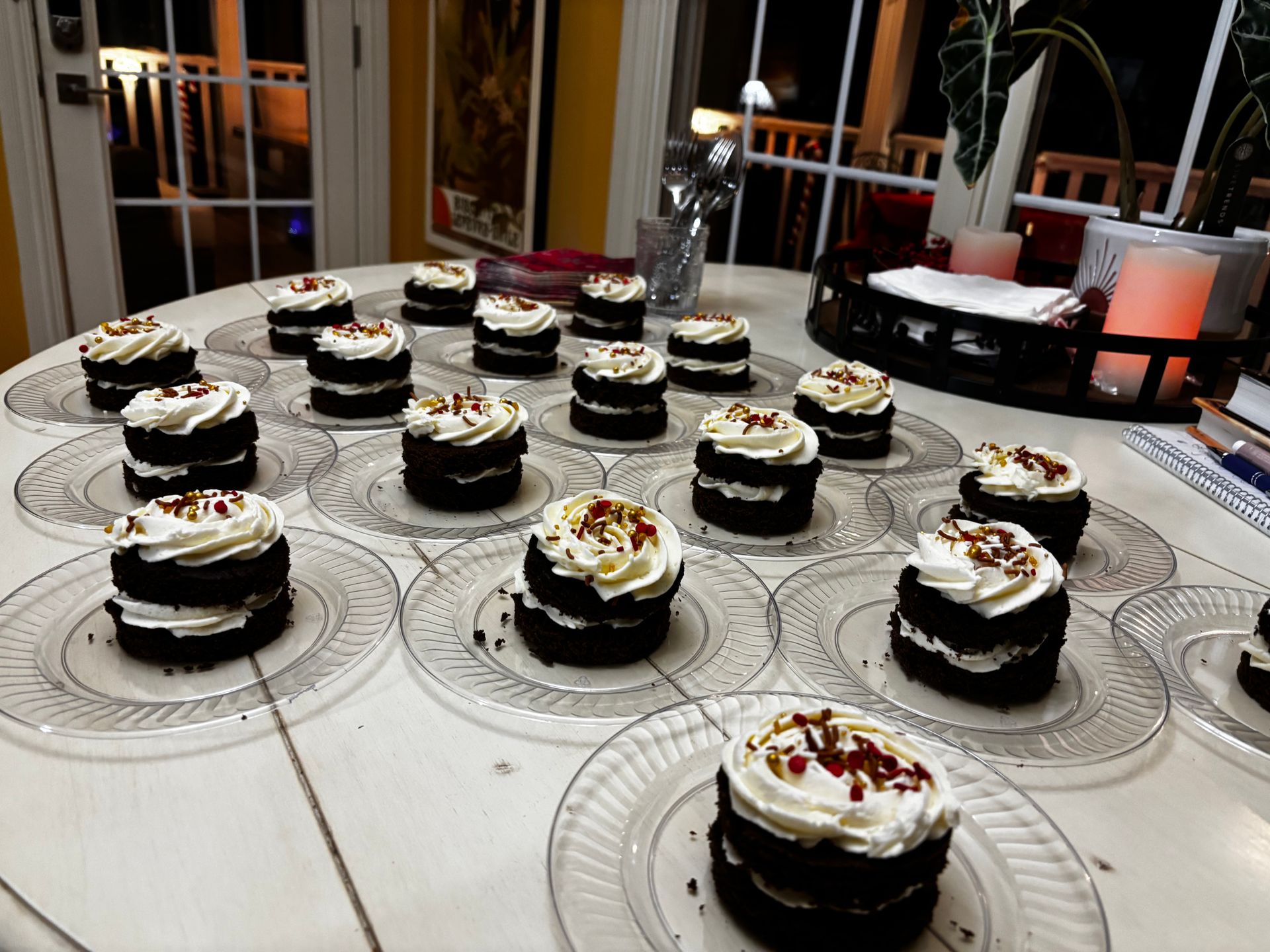Mini chocolate cakes with white frosting, arranged on clear plates on a white table.