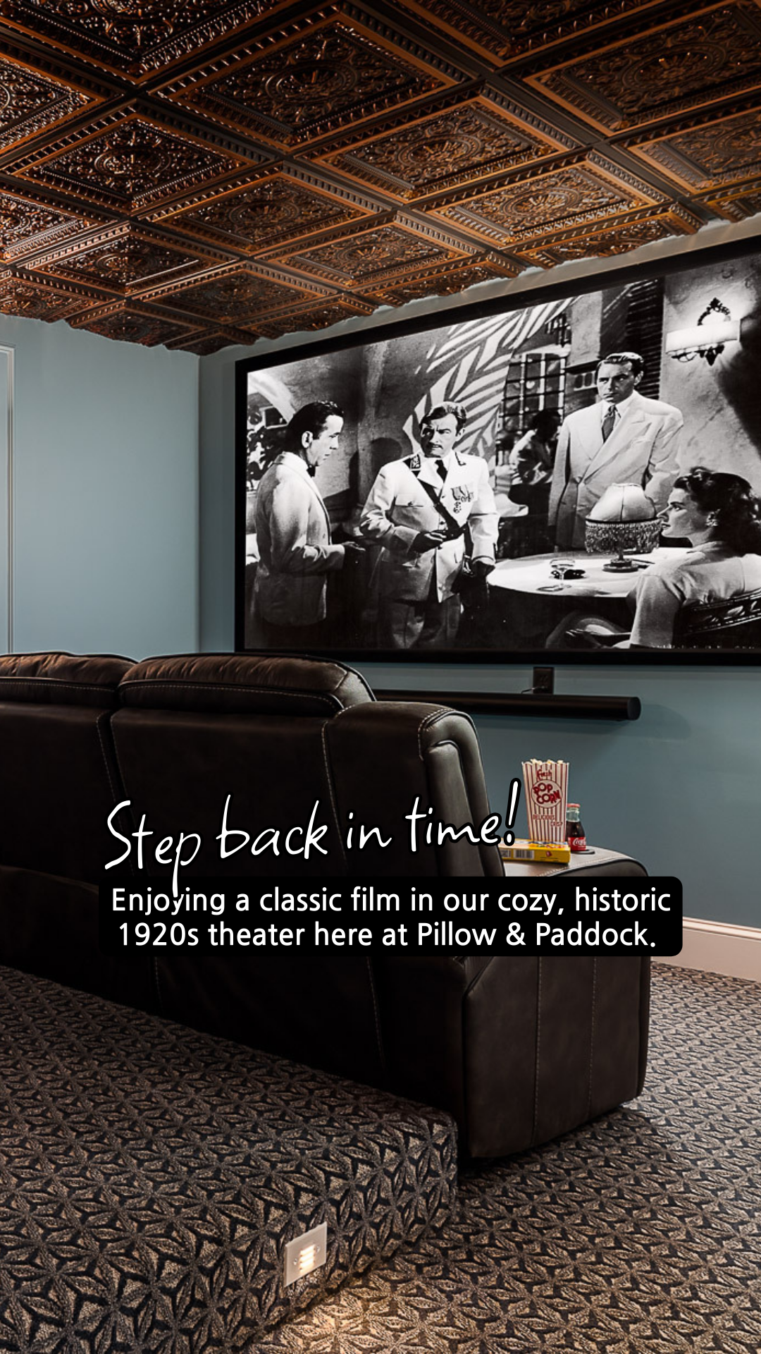 Cozy 1920s theater with a classic film playing on a large screen. Black leather couch, patterned ceiling.