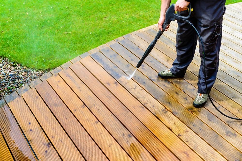 A Man Is Cleaning A Wooden Deck With A High Pressure Washer — Tall Orders Port Macquarie In Lake Cathie, NSW 
