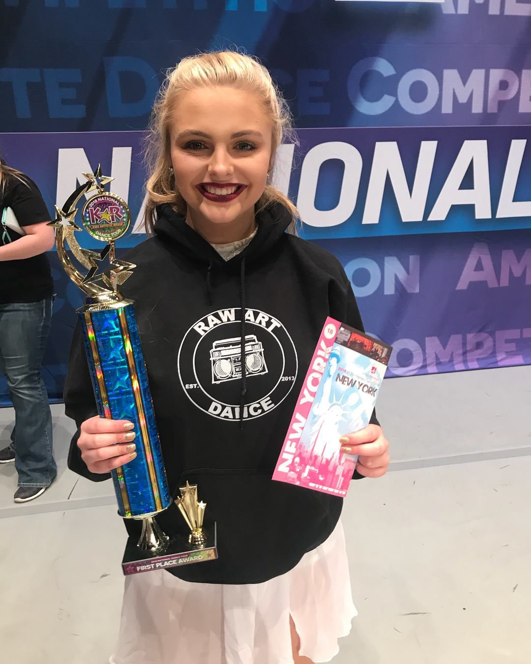 A woman is holding a trophy and a pamphlet.