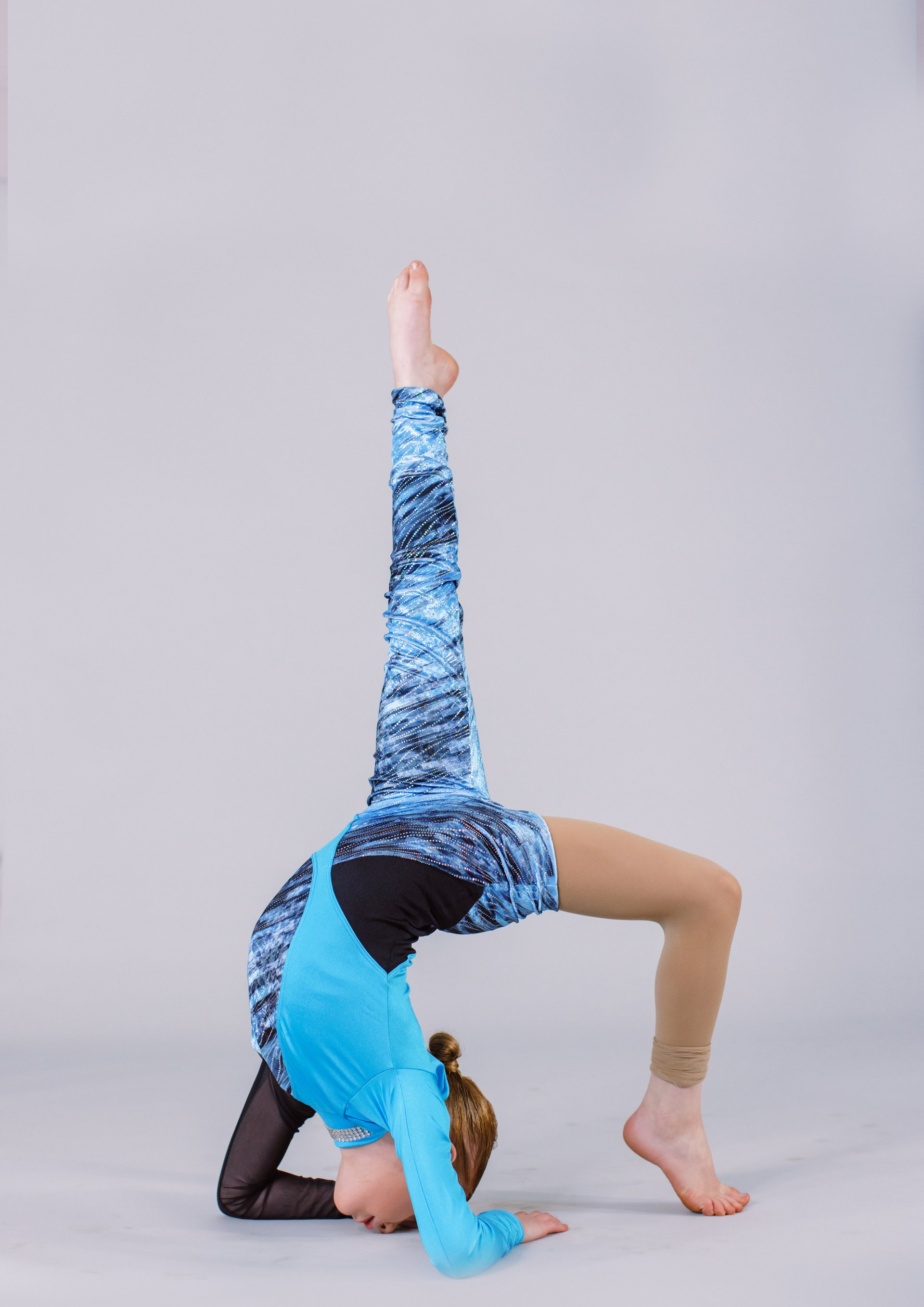 A young girl is doing a handstand with one leg up.