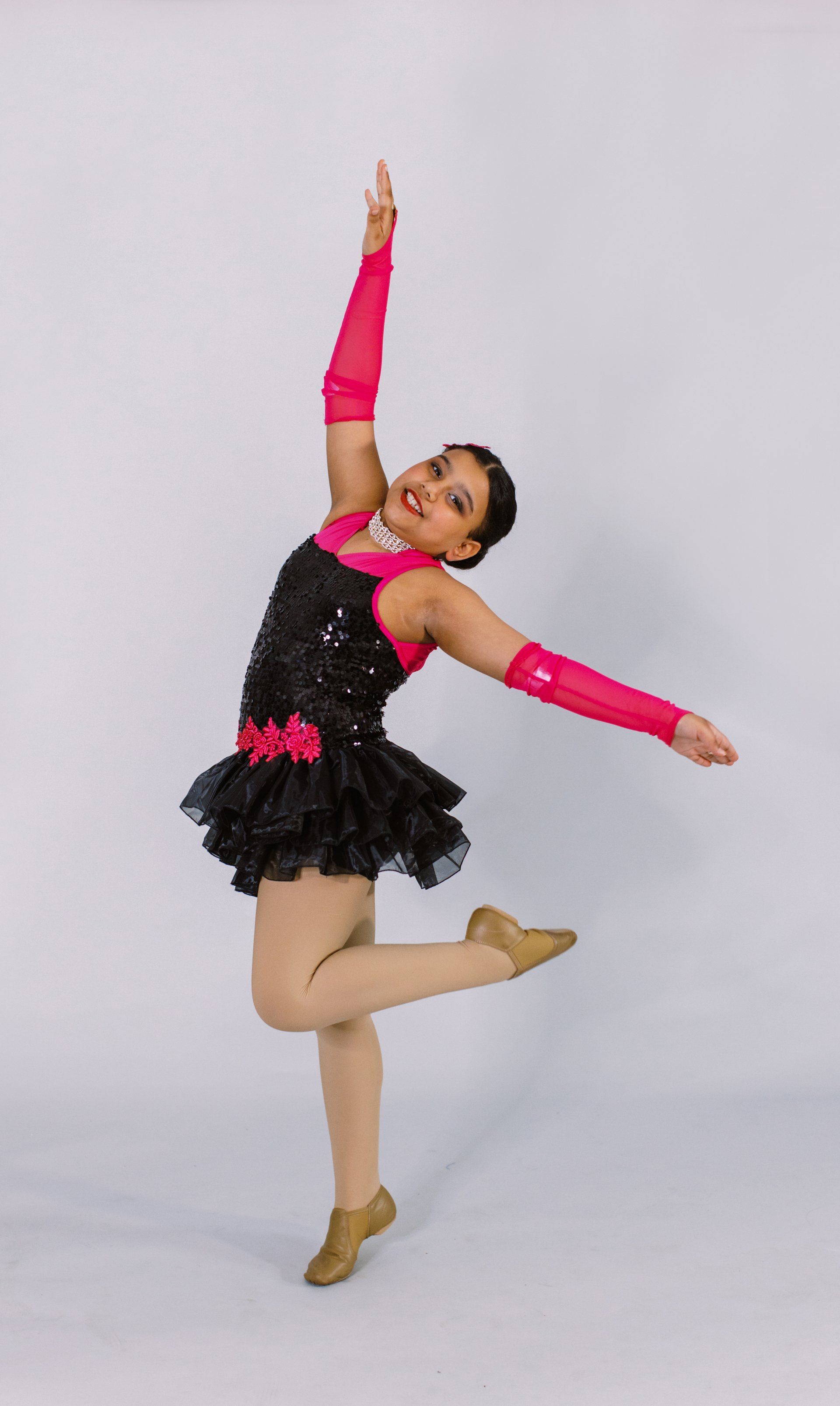 A young girl in a black and pink dress is dancing.