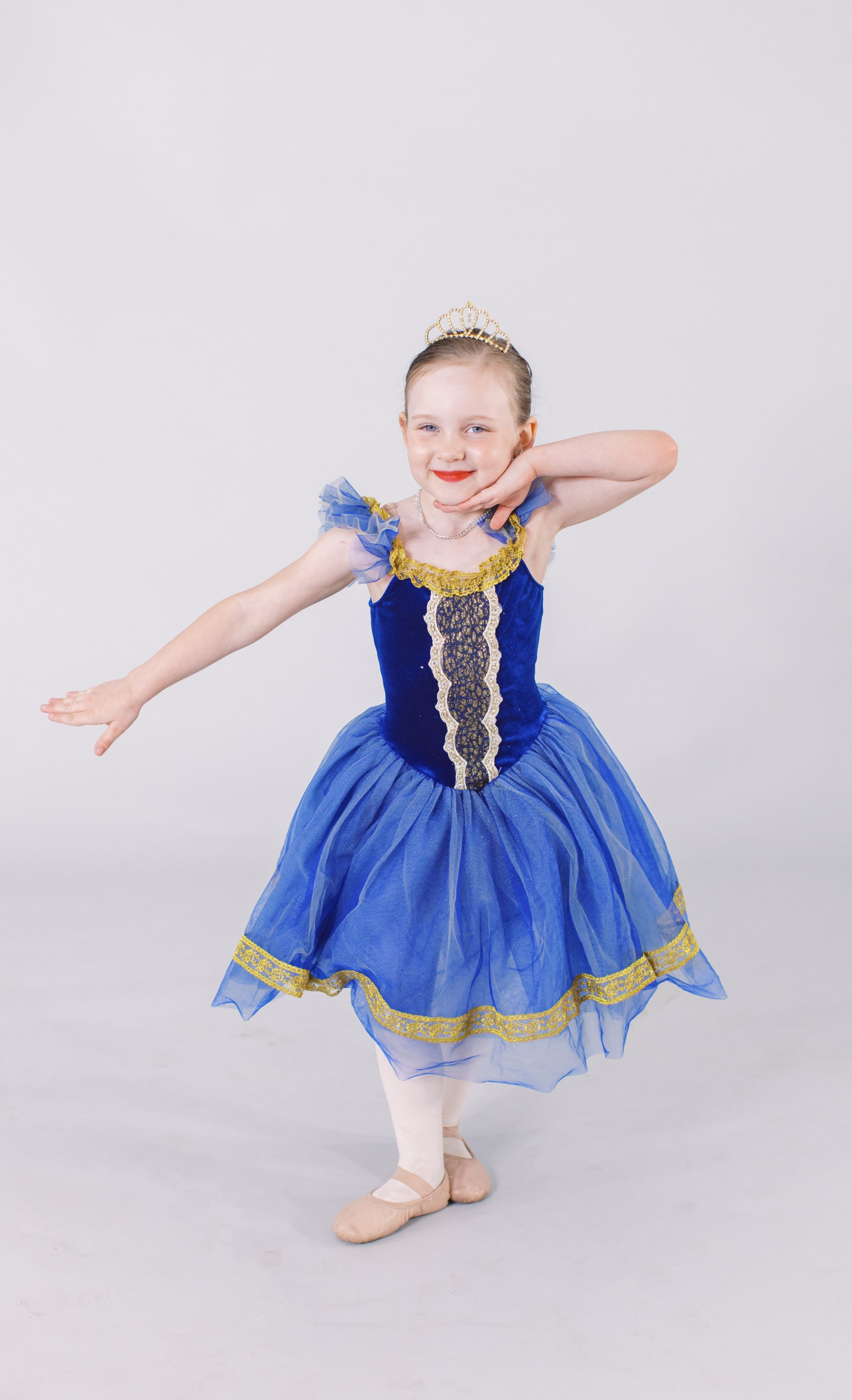 A little girl in a blue dress and tiara is dancing.