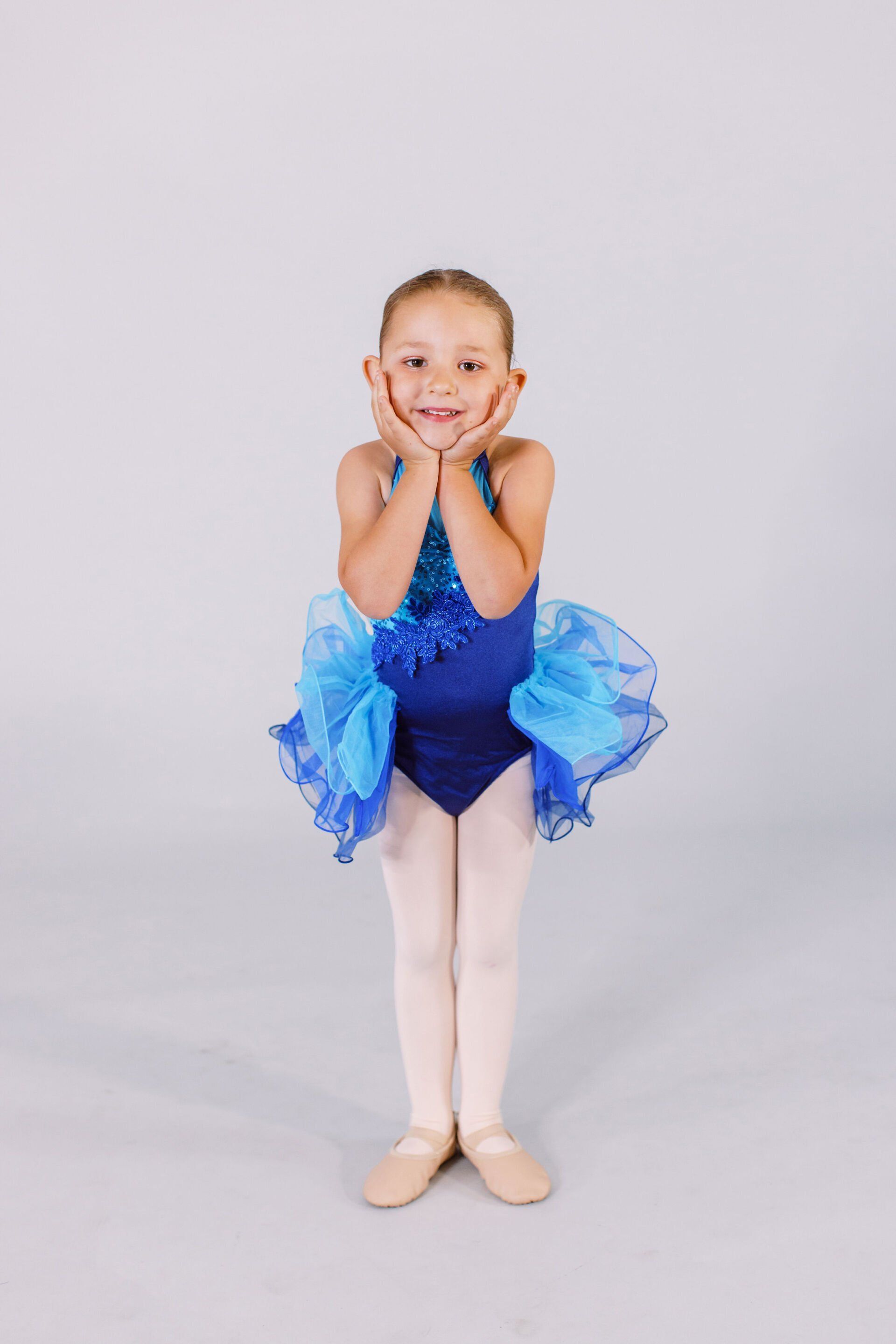 A little girl is wearing a blue leotard and tutu.