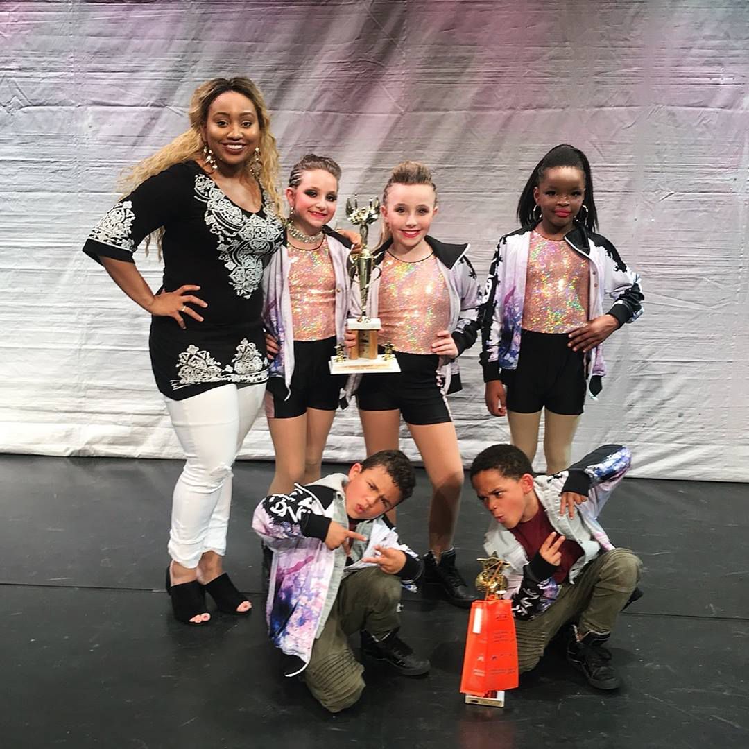 A group of young dancers are posing for a picture with a trophy.