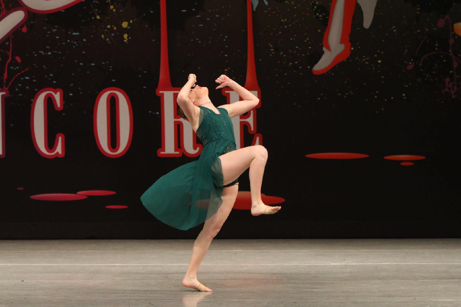 A woman in a green dress is dancing in front of a sign that says icon