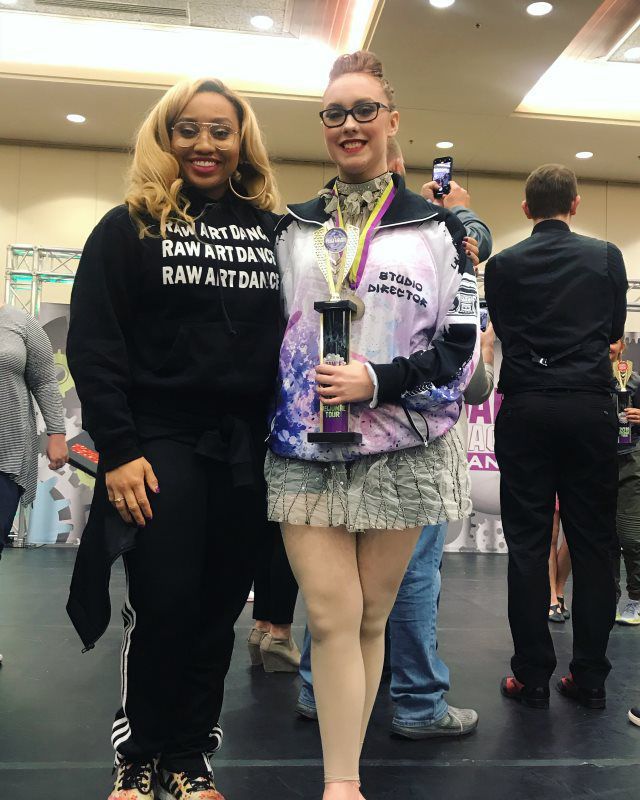 Two women are standing next to each other in a room holding trophies.