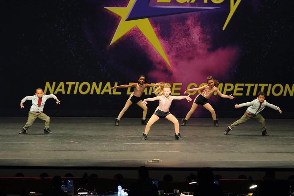 A group of people are dancing on a stage in front of a sign that says national dance competition.