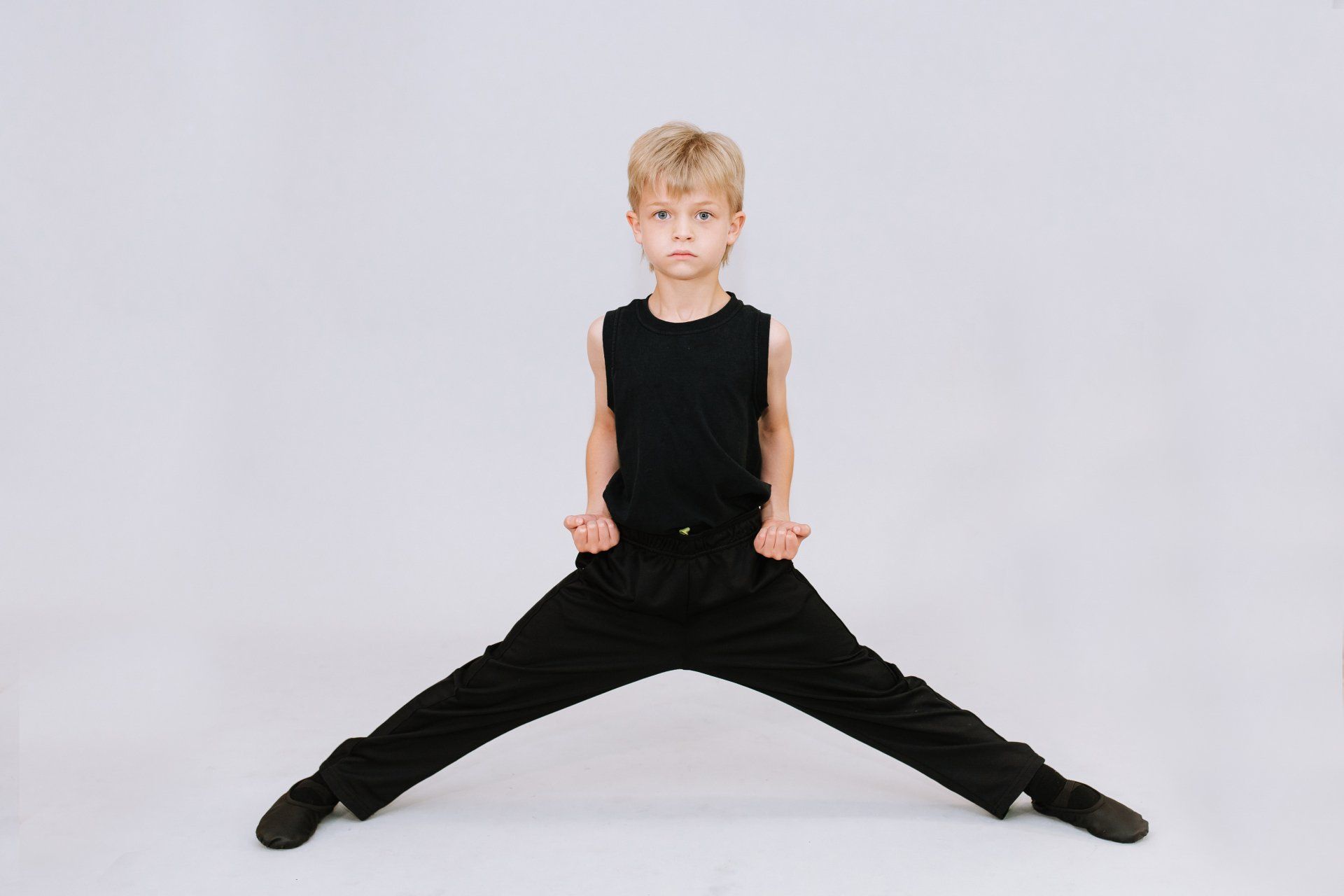 A young boy in a black tank top and black pants is sitting with his legs crossed.