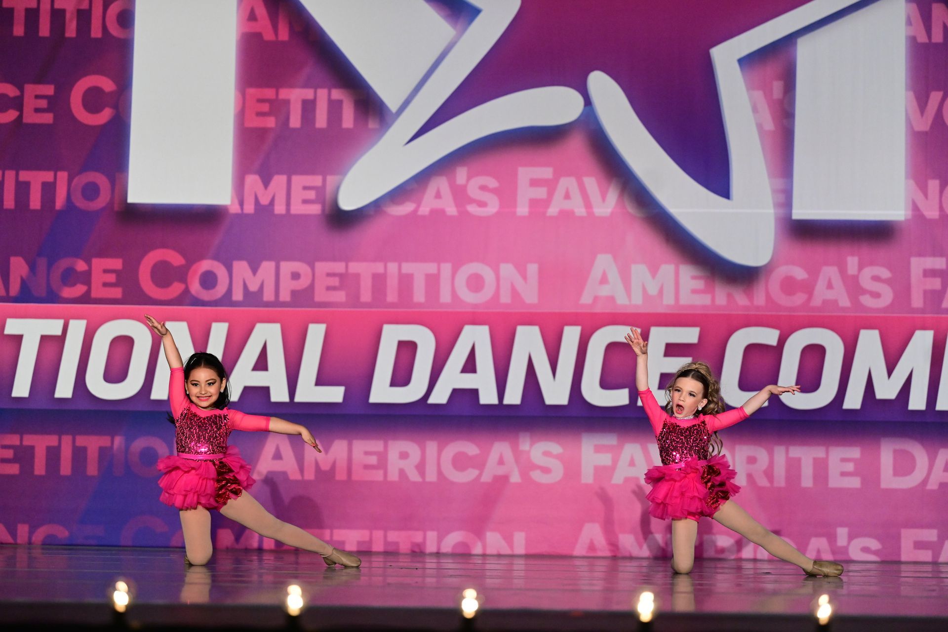 Two dancers in pink outfits perform on stage at a dance competition.