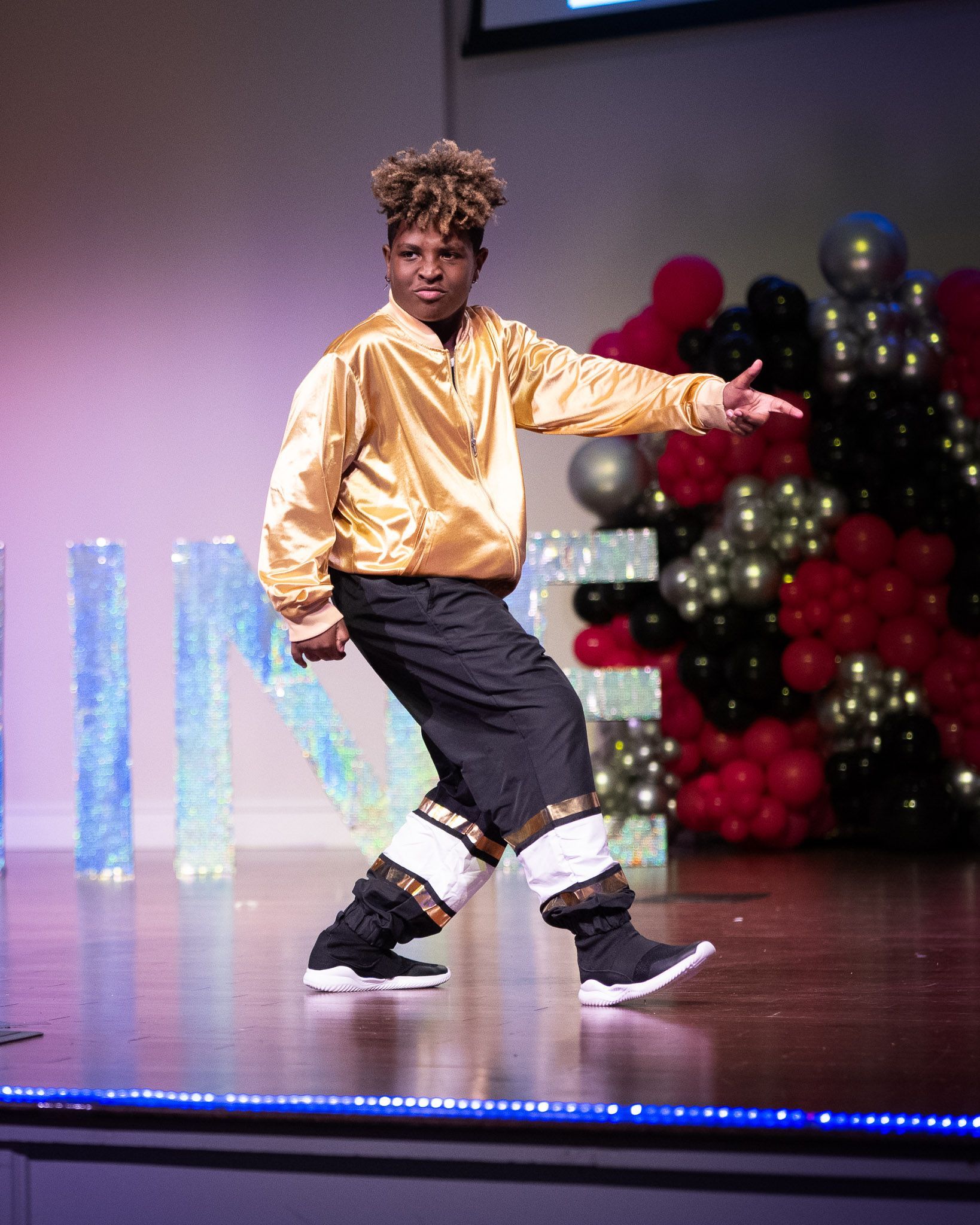 Young person in pink costume holds up flowing magenta fabric on stage. Large sparkly