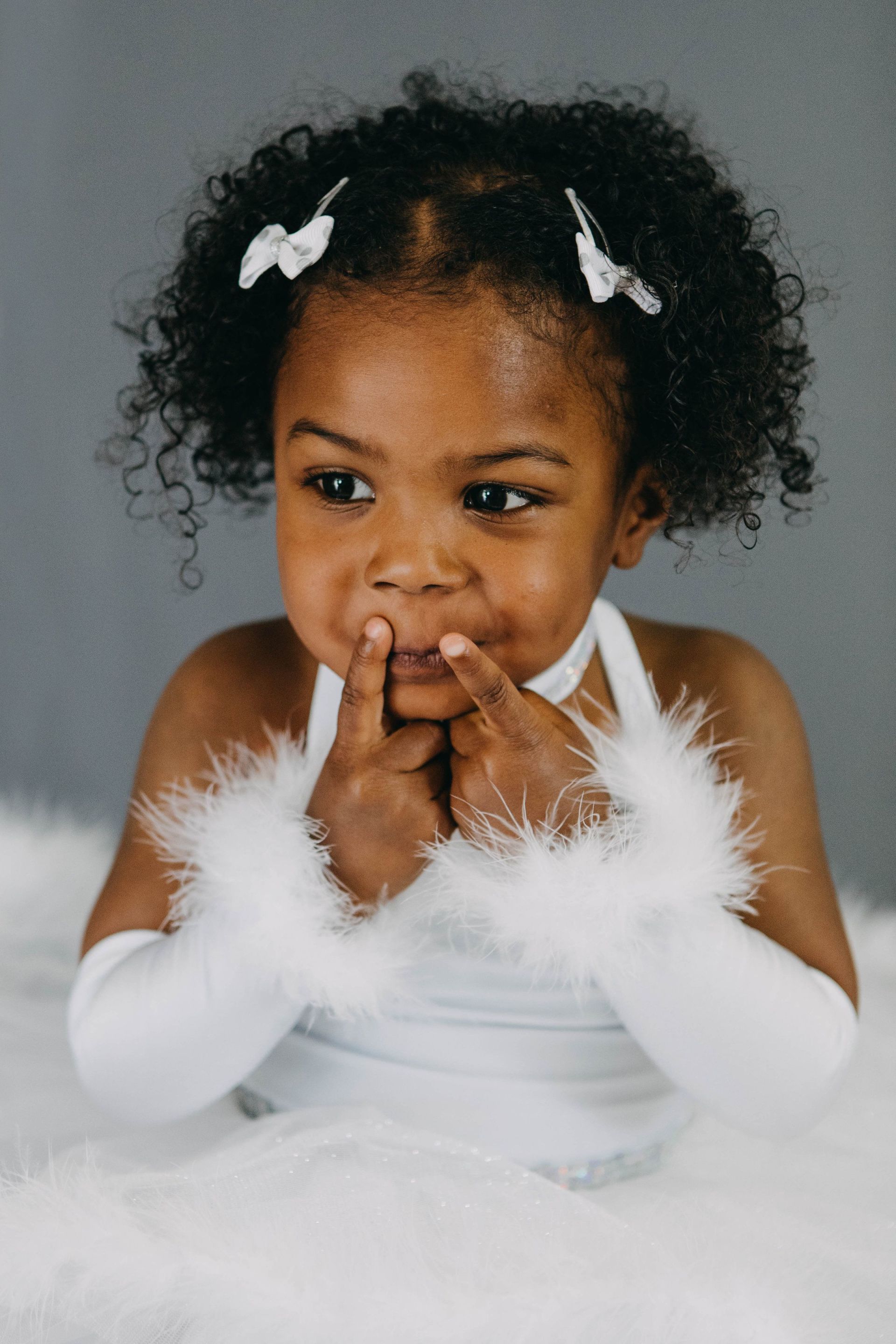 A little girl wearing white feathered gloves and a white dress