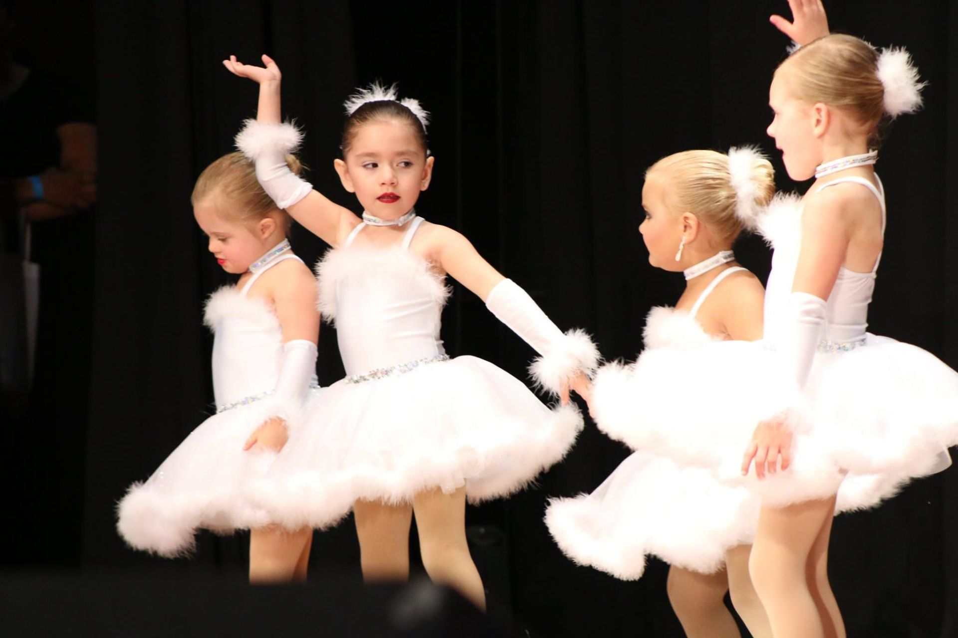 A group of young girls in white tutus are dancing on a stage