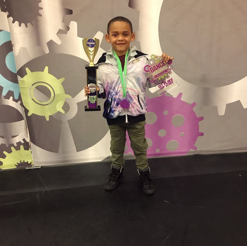 A young boy holding a trophy and a medal that says champions