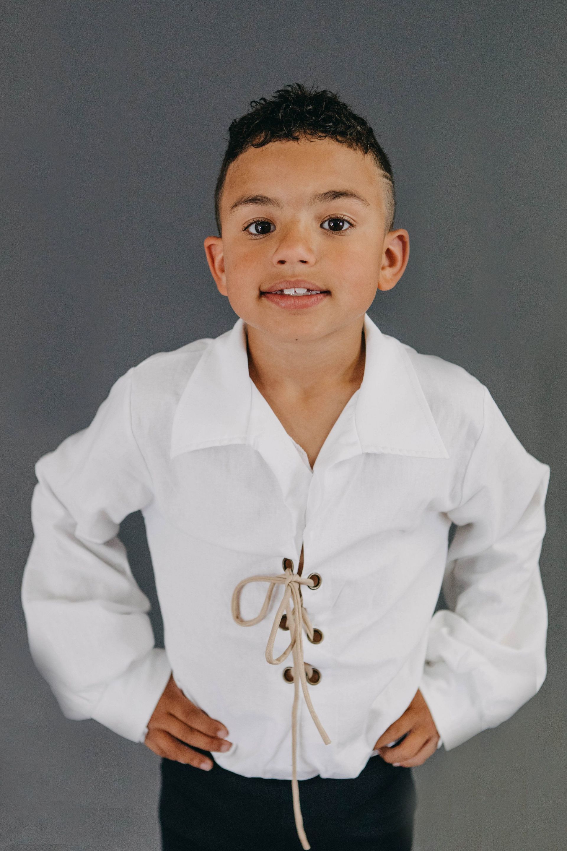 A young boy wearing a white shirt with a lace up front