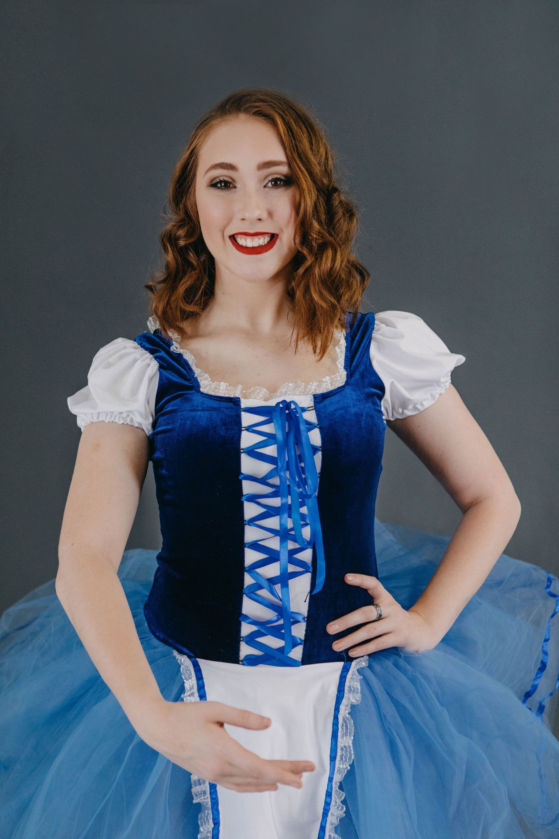 A woman in a blue and white costume is standing with her hands on her hips.