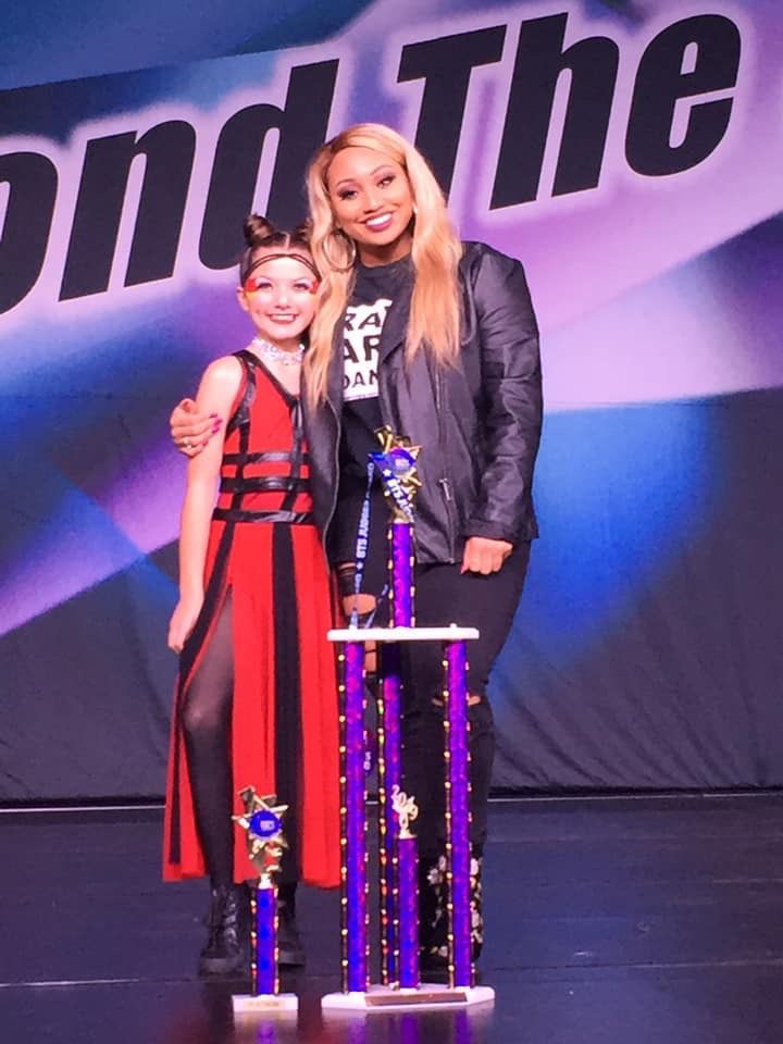 A woman and a girl are posing for a picture with trophies in front of a sign that says 