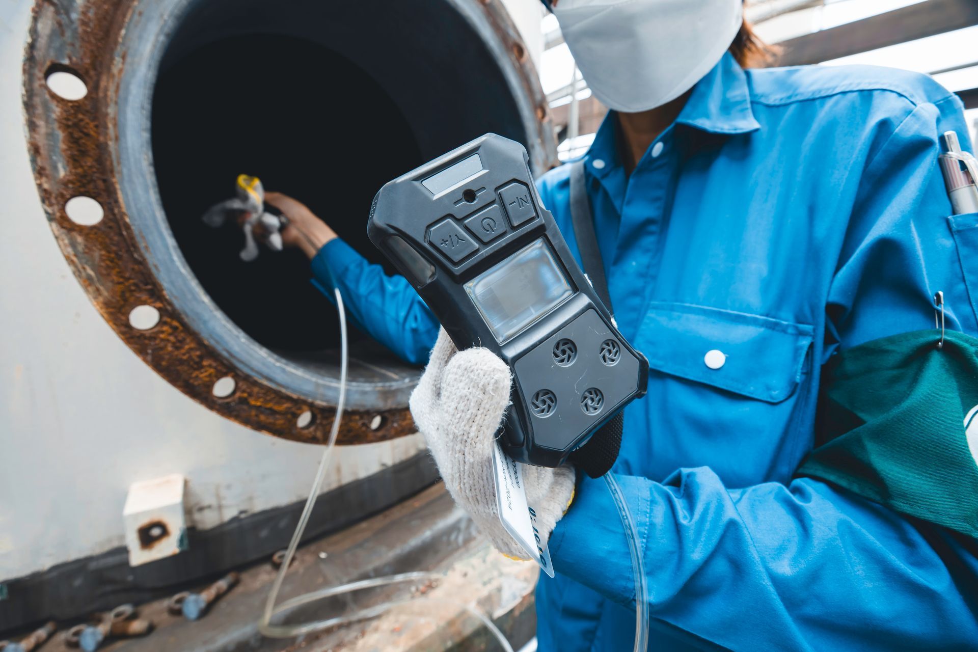 A technician in protective gear conducts emissions testing at an industrial pipe opening.