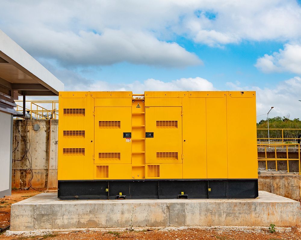 Yellow industrial generator on concrete platform against a blue sky with clouds.