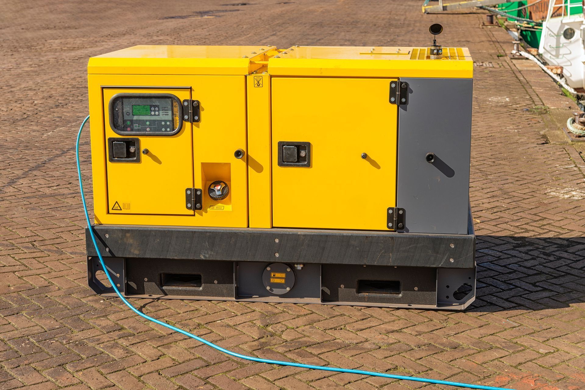 Yellow and gray generator on a paved surface, blue cable extending.