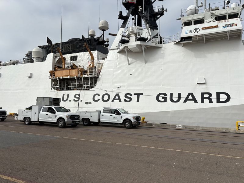 A U.S. Coast Guard cutter docked with utility trucks parked alongside.