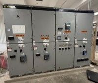 A four-section grey industrial electrical switchgear cabinet with various meters, switches, and labels.