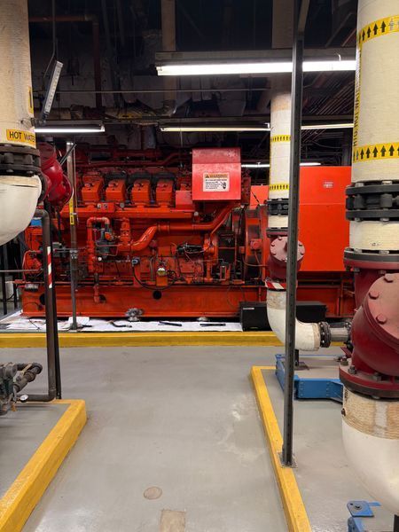 Large orange industrial machinery in a utility room, surrounded by pipes and equipment.
