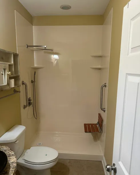 Accessible walk-in shower with grab bars, bench, handheld shower, and toilet in a small bathroom.