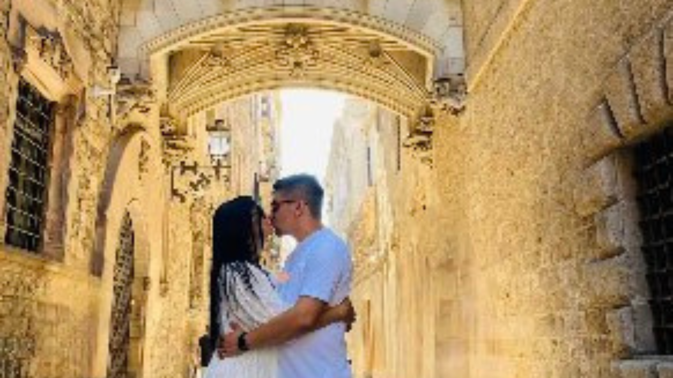 A romantic couple sharing a kiss under the iconic Bishop Bridge in the Gothic Quarter of Barcelona.