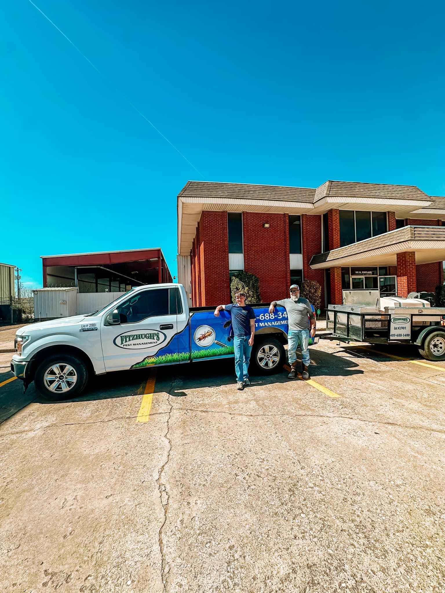 Two men are standing next to a truck in a parking lot in front of a building.