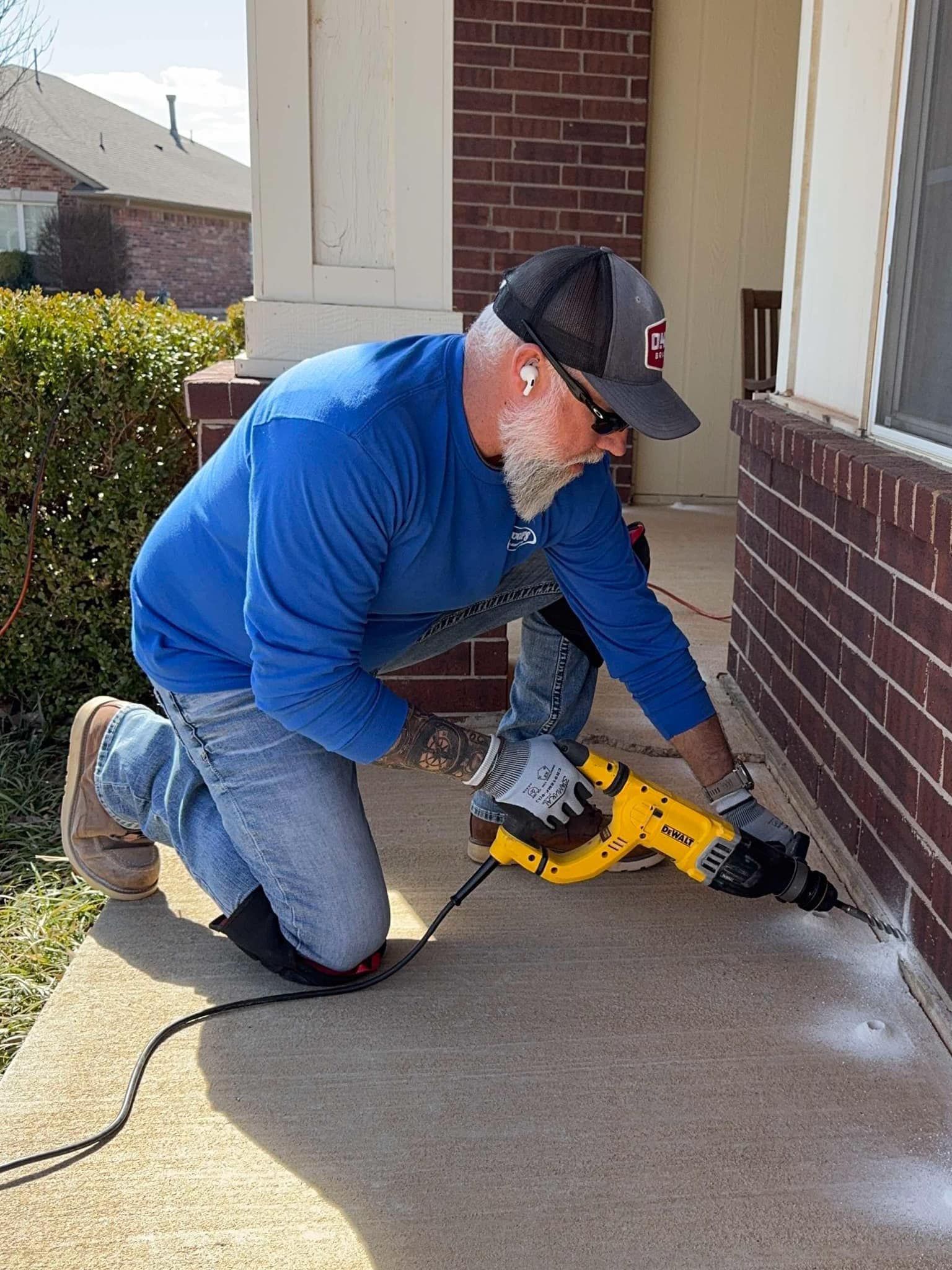 A man is kneeling down with a drill in front of a brick building.