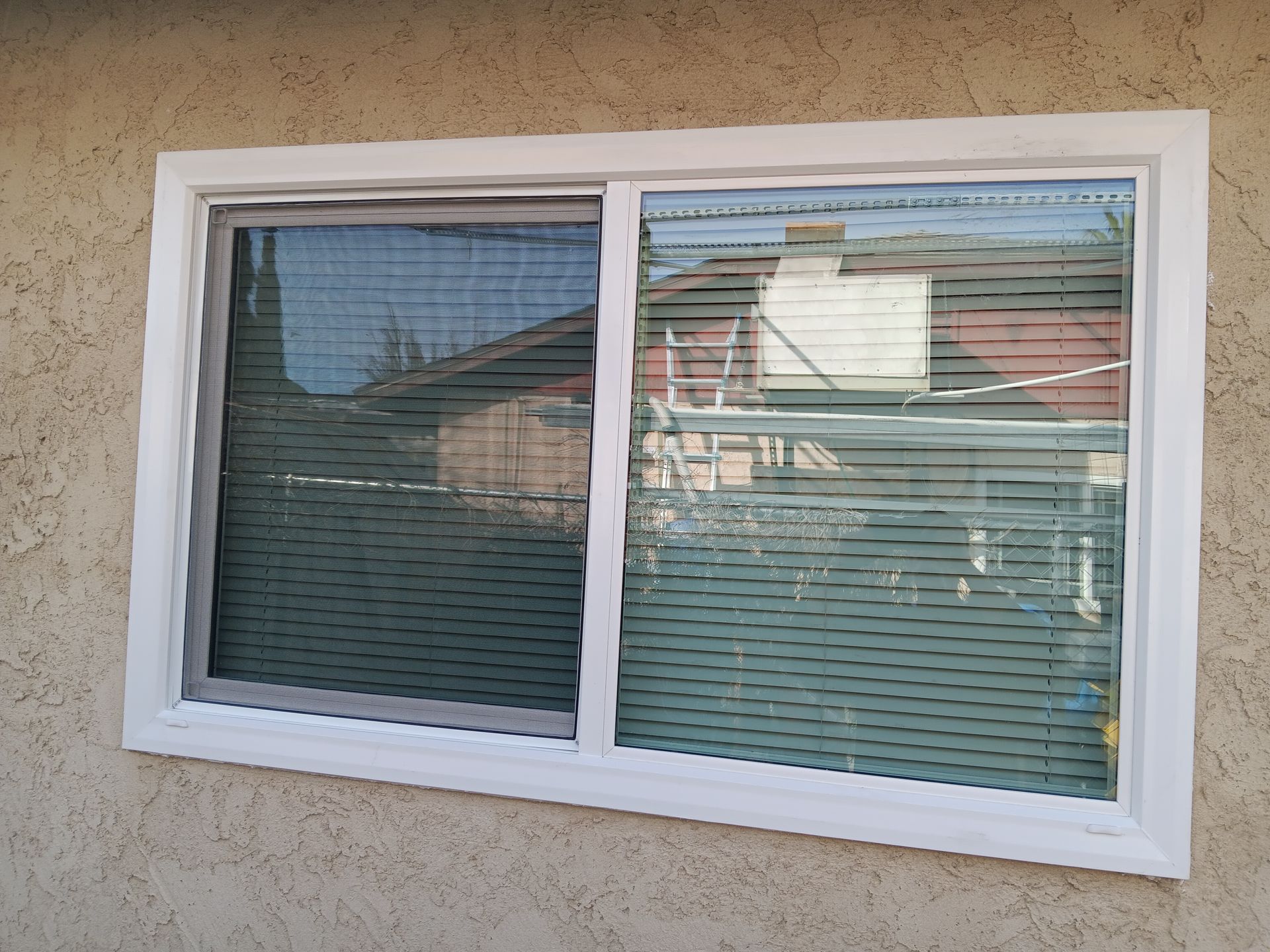 Person using a screwdriver to install a window. White frame, gray gloves, window screen visible.