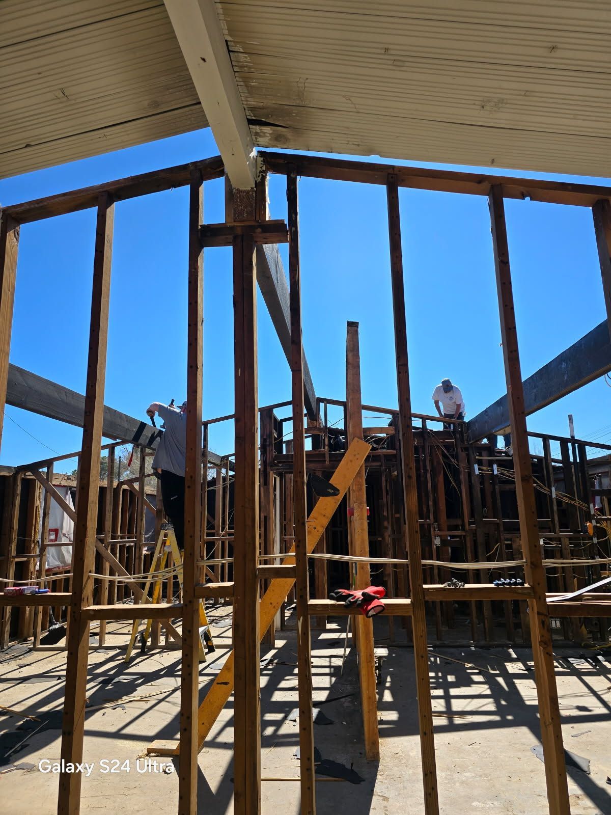 Construction workers building a wooden structure under a bright blue sky.